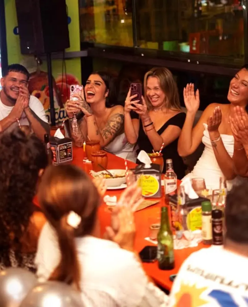 Grupo celebrando en una mesa de D'Corner, con globos y aplausos de fondo