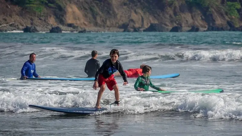 Clase en la orilla con alumnos y tablas de colores entre las olas