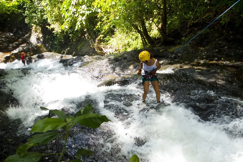 Persona descendiendo en rappel por una catarata entre rocas y vegetación