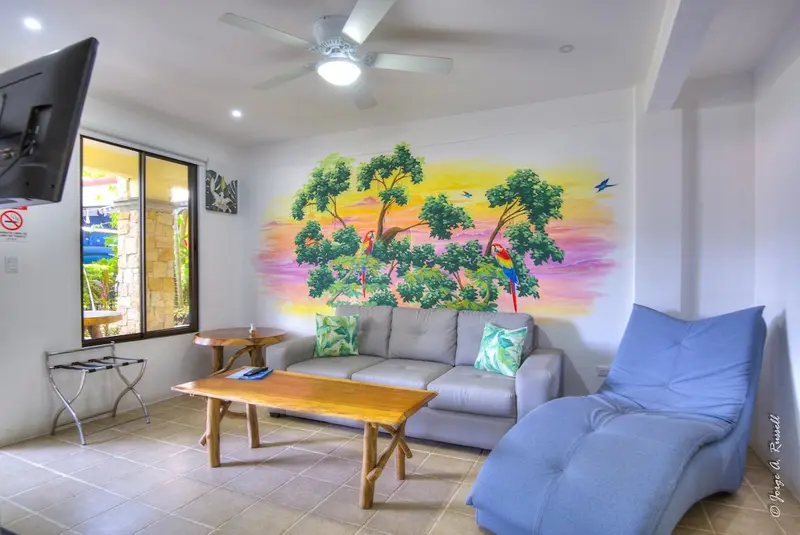 Sala con mural de playa, mesa de centro de madera y sillón azul junto a ventanales