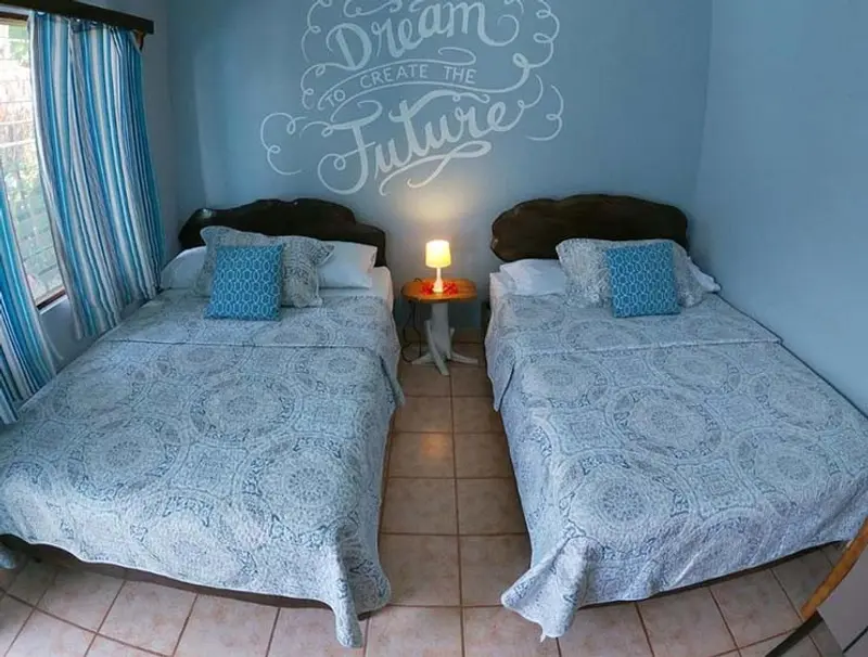 Habitación twin con dos camas dobles de colcha celeste, lámpara en la mesa de noche y cortinas azules