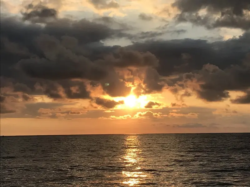 Sol poniéndose entre nubes oscuras sobre el mar, con su reflejo en el agua