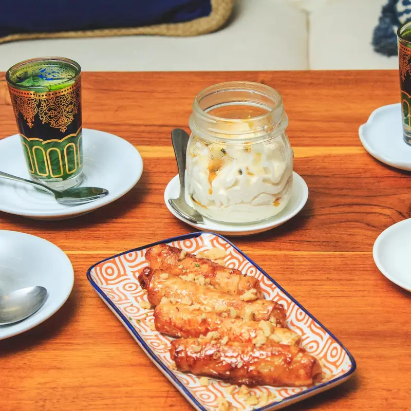 Schnitzel en una fuente decorada junto a un vaso de té de menta y un frasco con postre cremoso