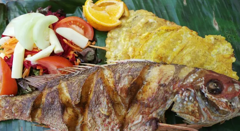 Pargo entero frito sobre una hoja de plátano, con patacón, ensalada de pepino, tomate y zanahoria