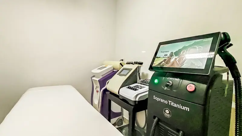 Sala de tratamiento con camilla blanca y equipos de depilación láser y cavitación