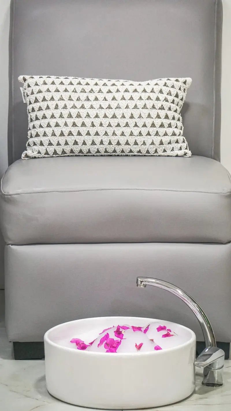 Sillón gris con almohada y pediluvio blanco con pétalos de flores