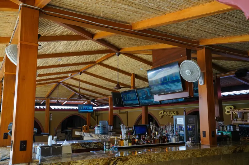 Barra con techo de bambú y madera, botellas y televisores en el bar al aire libre