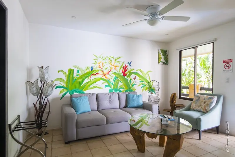 Sala con sofá gris, mesa de vidrio y plantas junto a la ventana, con ventilador de techo