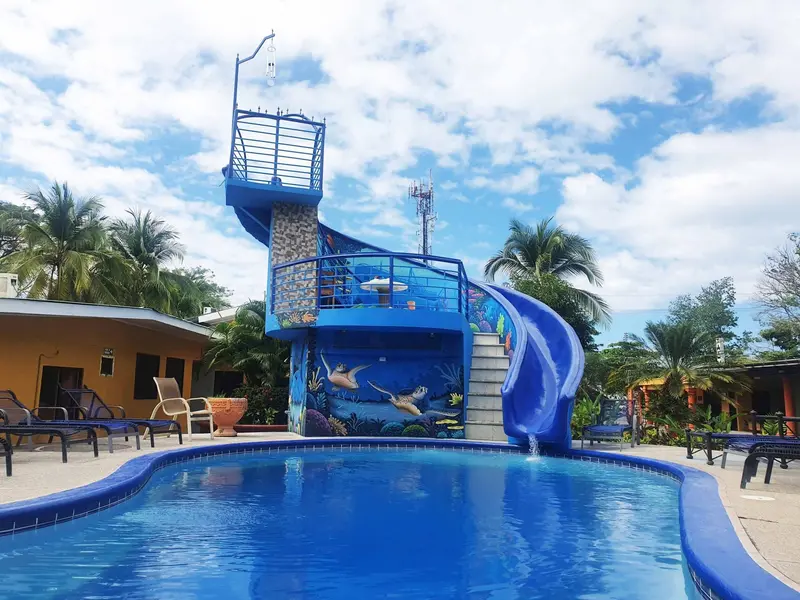 Piscina con torre de tobogán azul y murales marinos junto a los cuartos del hotel