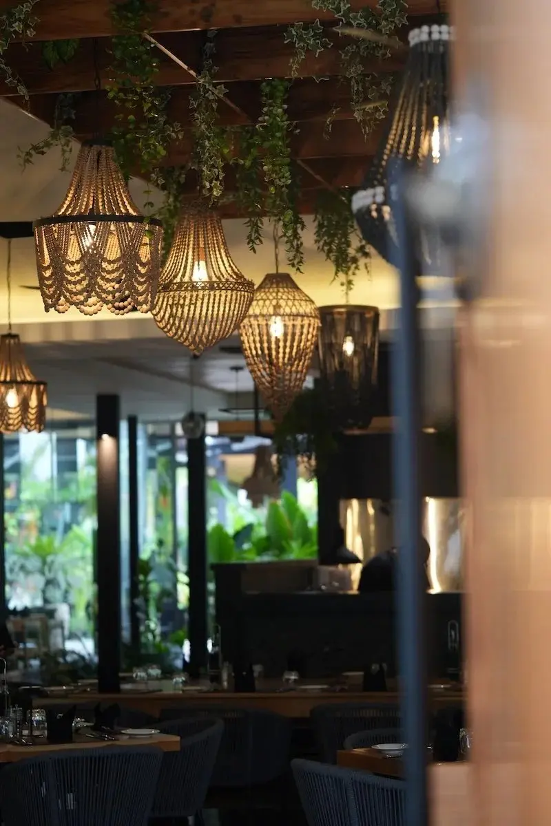Lámparas colgantes de fibra y plantas sobre el salón, con mesas al fondo