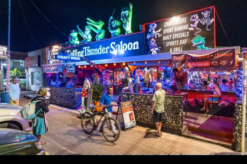 Fachada del bar de noche con luces de colores y una bicicleta estacionada al frente