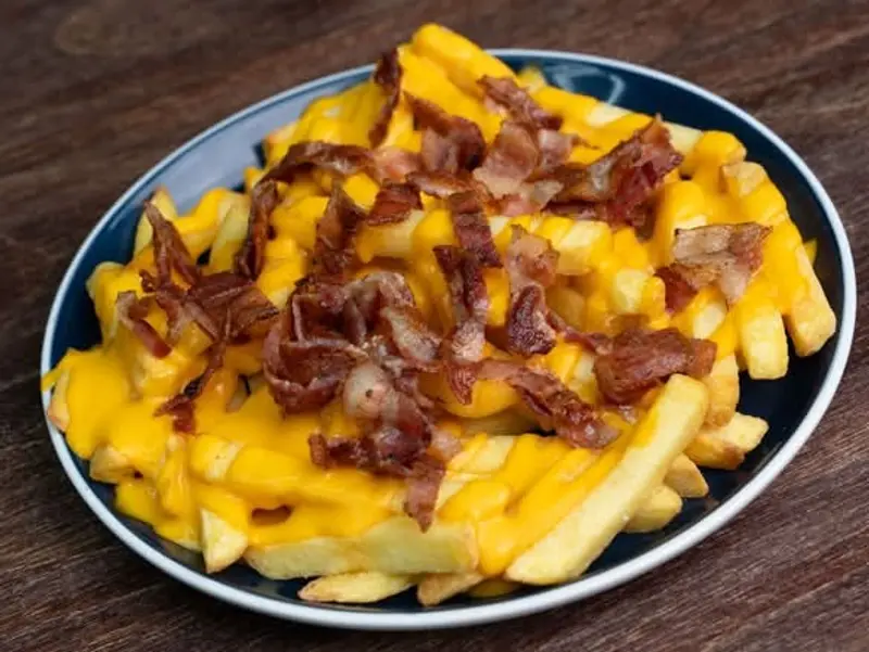 Bacon Fries: papas con salsa de queso cheddar y tocino crocante en un plato azul