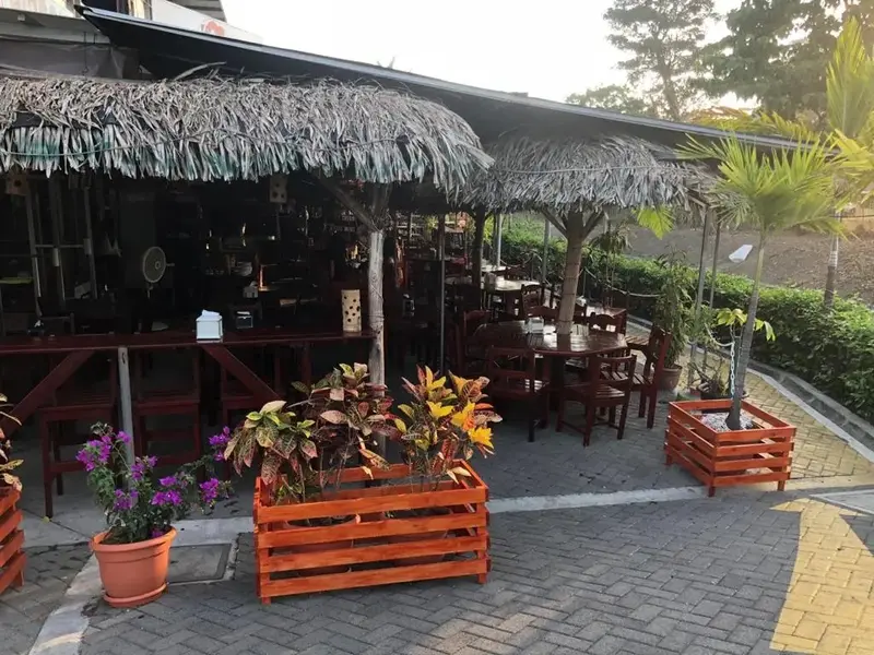 Terraza con techo de palma, mesas y sillas de madera y macetas con flores