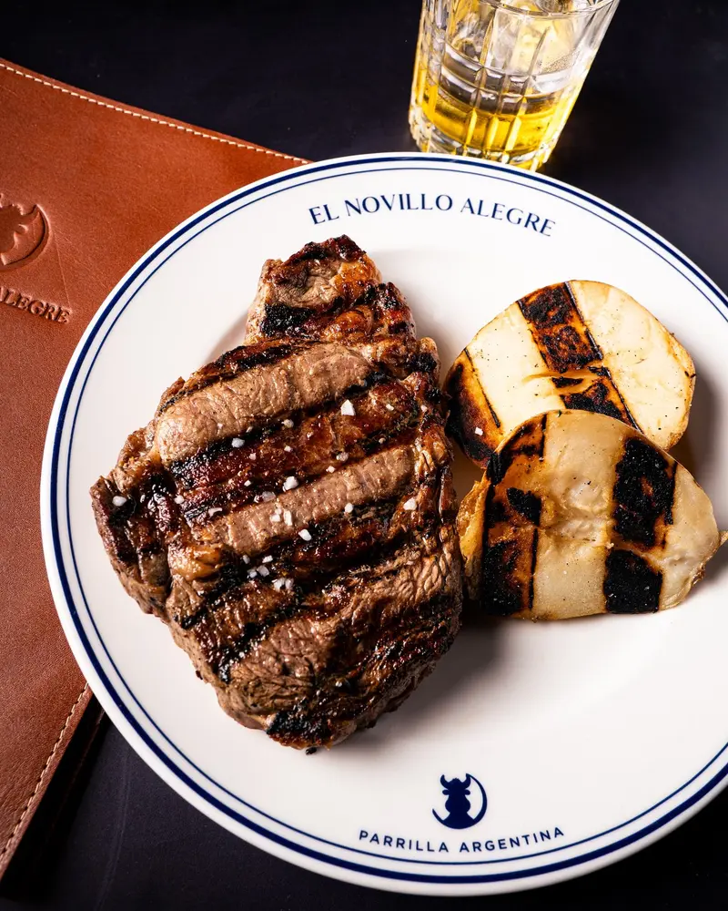 Corte de carne a la parrilla con rodajas asadas en un plato blanco con el logo de El Novillo Alegre