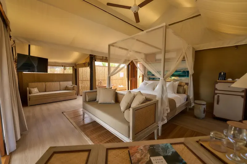 Dormitorio con cama con dosel, sala con televisor y paredes de lona claras