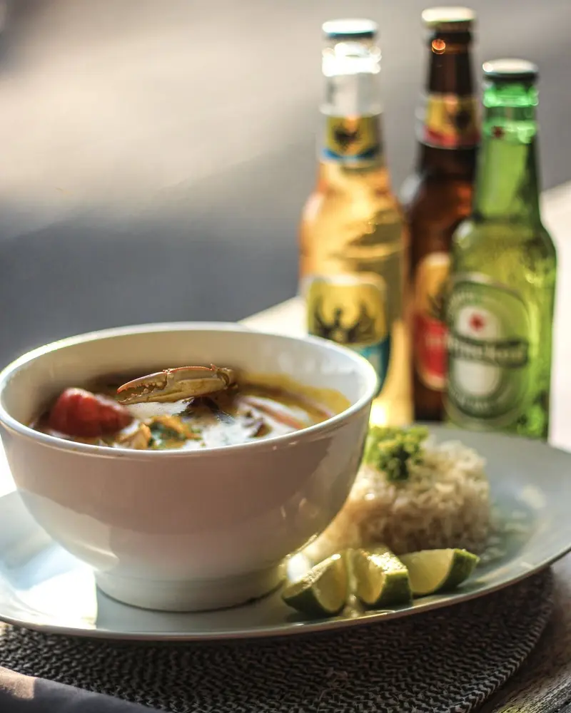 Sopa de mariscos en un tazón con arroz, limones y tres botellas de cerveza al fondo