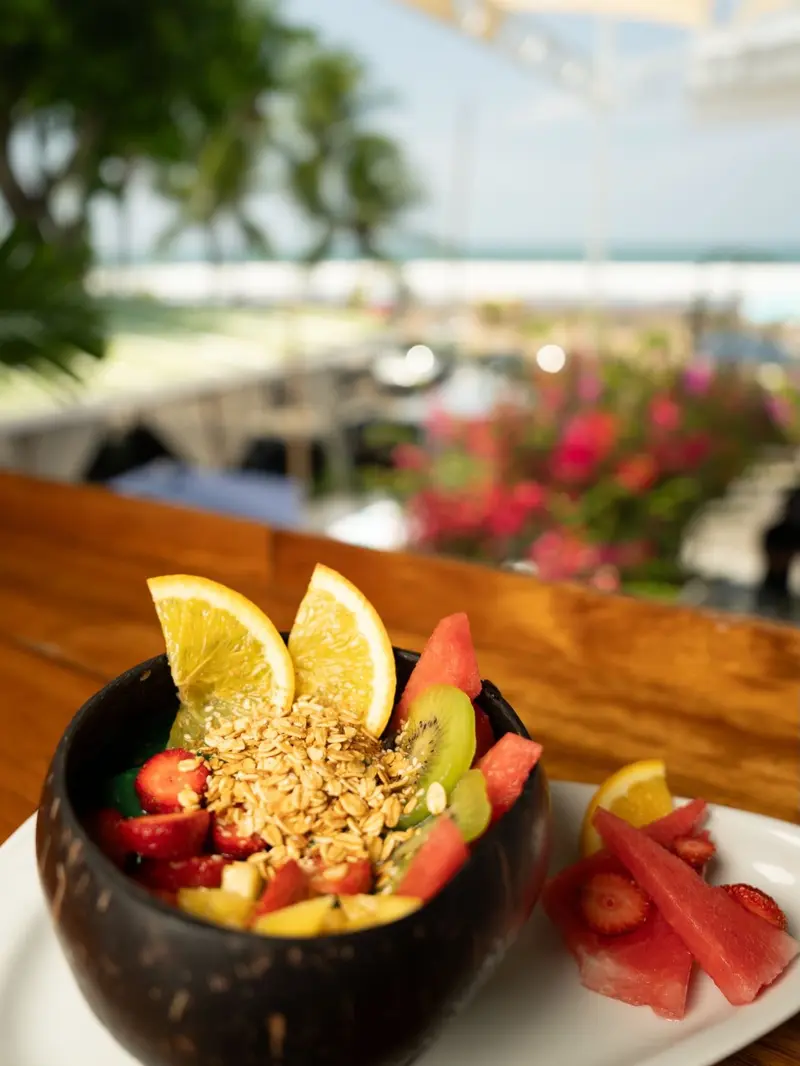 Bowl de fruta con granola servido en un coco sobre la barra frente al mar