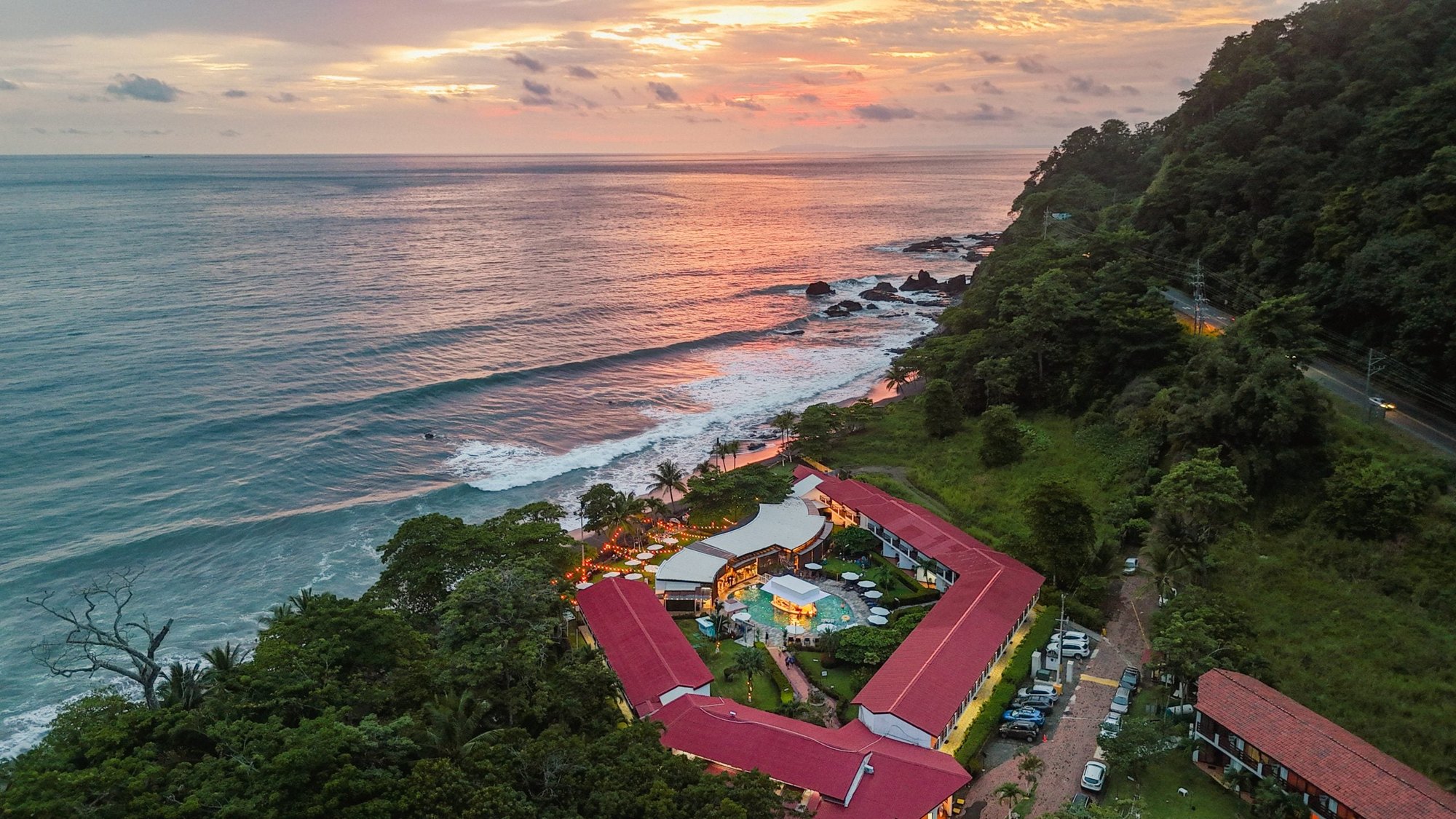 Vista aérea de la costa de Playa Hermosa al atardecer con un hotel de techos rojos