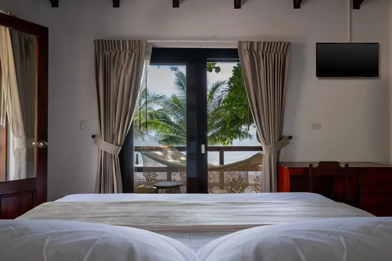 Cama king frente a la puerta de vidrio con balcón y vista a las palmeras