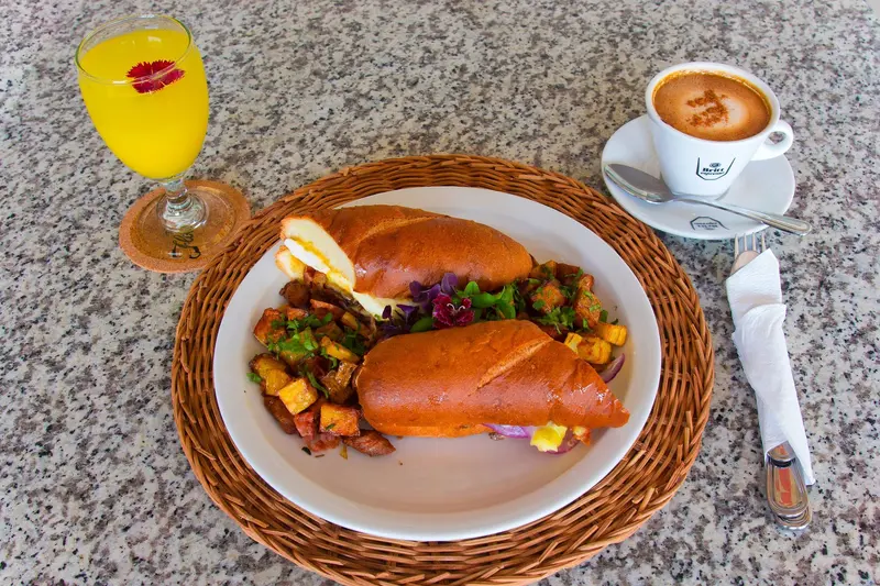 Desayuno sobre un individual de mimbre: pan con papas y verduras salteadas, un vaso de jugo de naranja y un café