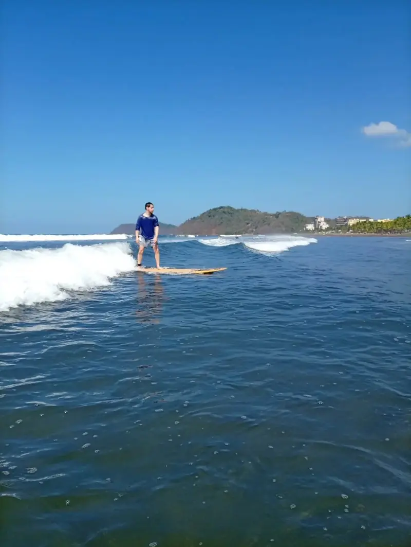 Surfista en una ola ancha de aguas azules frente a la costa