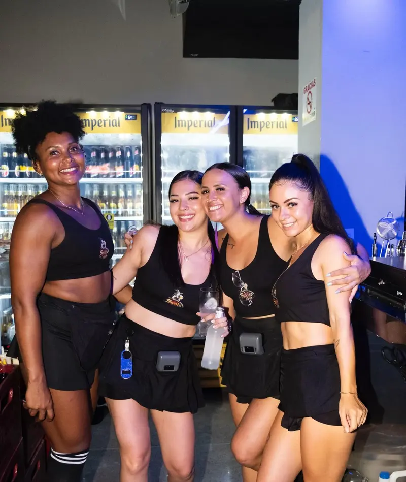 Cuatro integrantes del equipo de Spells con tops y faldas negros, sonriendo frente a la barra