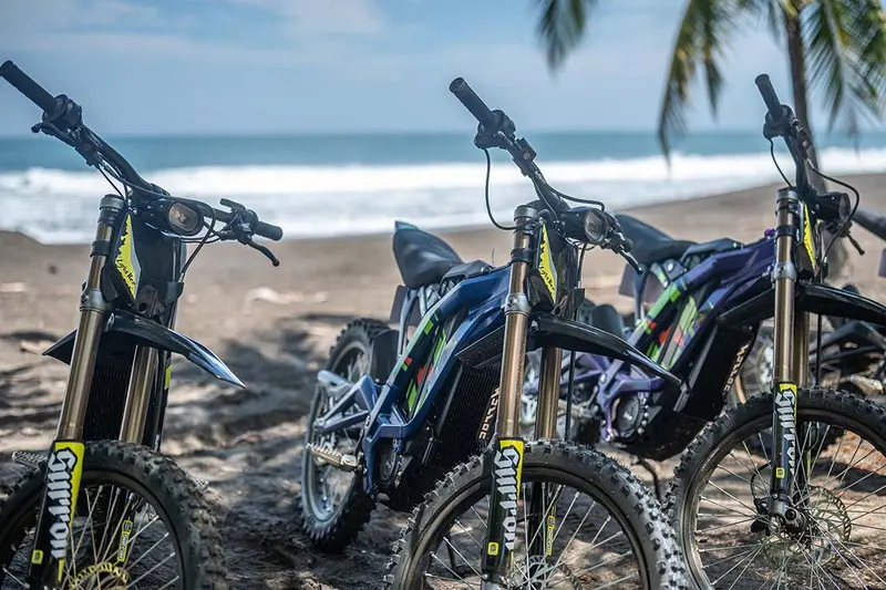 Tres motos eléctricas estacionadas en la arena de una playa de arena oscura