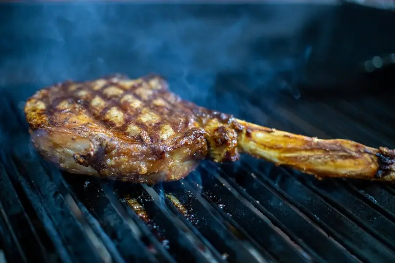 Corte Tomahawk dorándose sobre la parrilla, con humo azulado detrás
