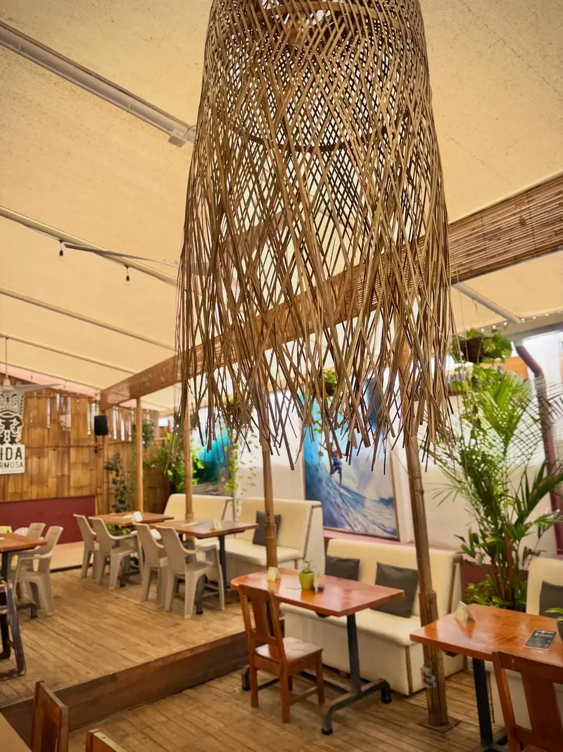 Vida Hermosa's indoor dining area, with a woven rattan lamp and a surf mural in the background