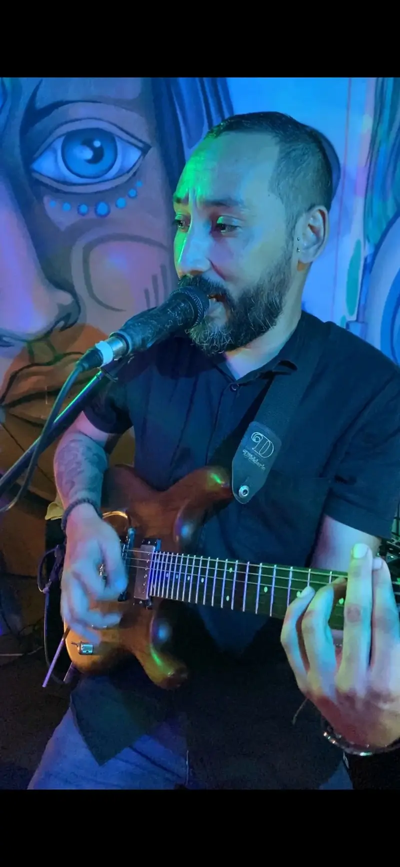 Guitarrista tocando y cantando frente a un mural de ojos y colores
