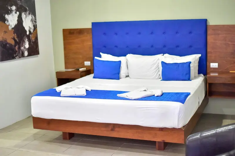 Habitación con cama de cabecera azul tapizada, mesas de noche de madera y una segunda cama
