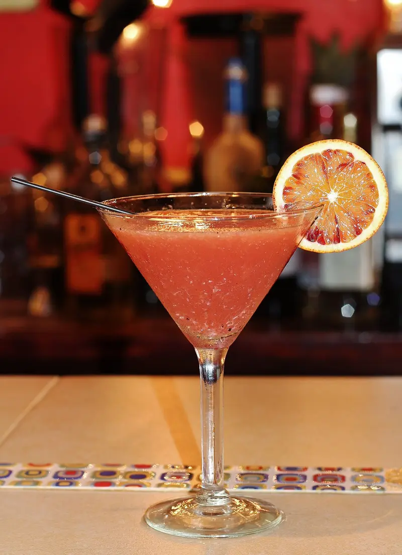 Cóctel rosado en copa de martini con una rodaja de cítrico