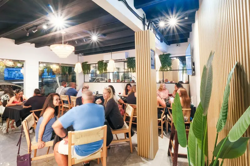 Comedor lleno de comensales bajo lámparas de madera y plantas