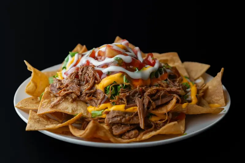 Nachos con carne mechada, queso, crema agria y pico de gallo sobre un plato blanco