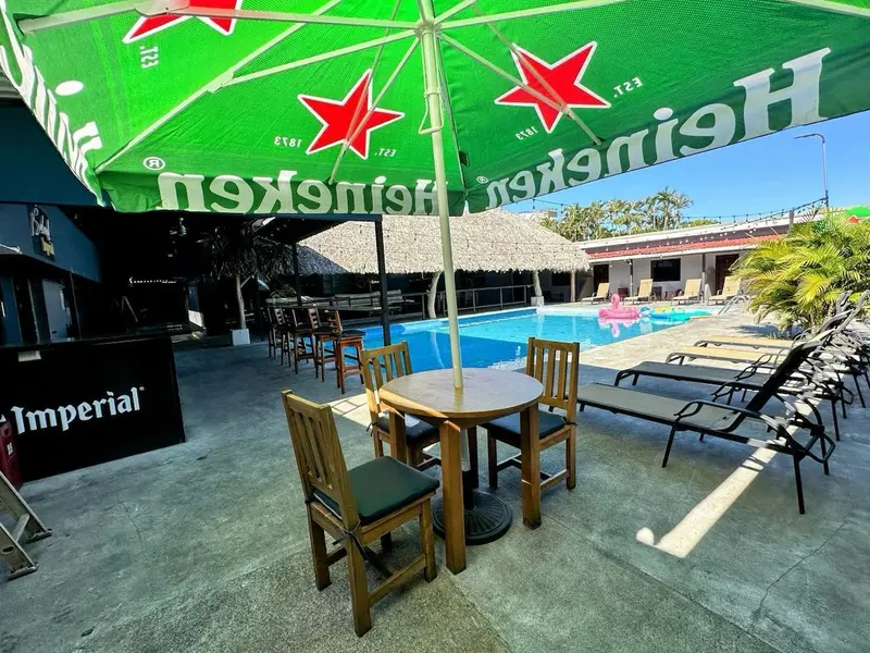 Mesa redonda de madera bajo una sombrilla verde junto a la piscina y las tumbonas