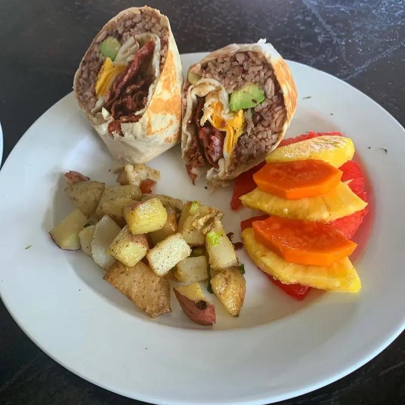 Burrito partido con carne y aguacate, papas salteadas y fruta fresca en un plato blanco