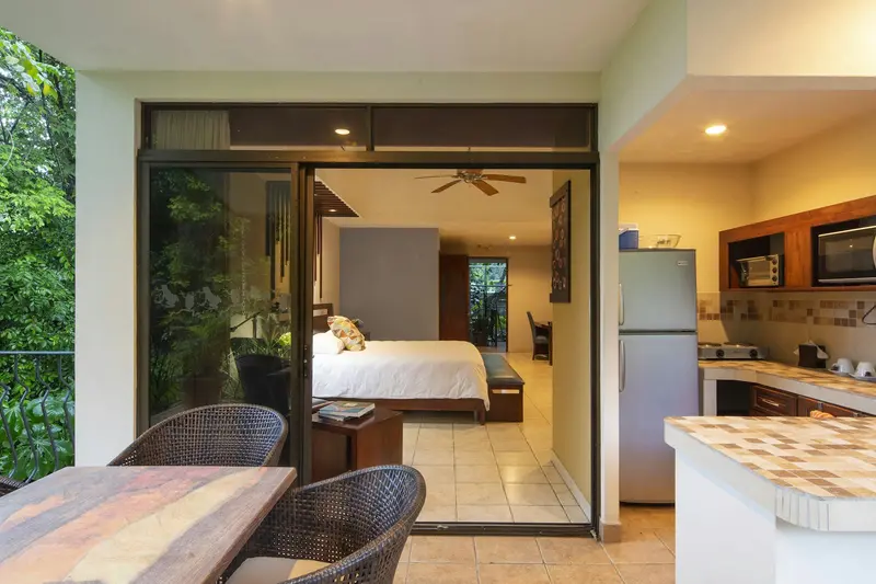 Terraza de una suite con mesa y sillas de ratán, cocina equipada y la habitación al fondo