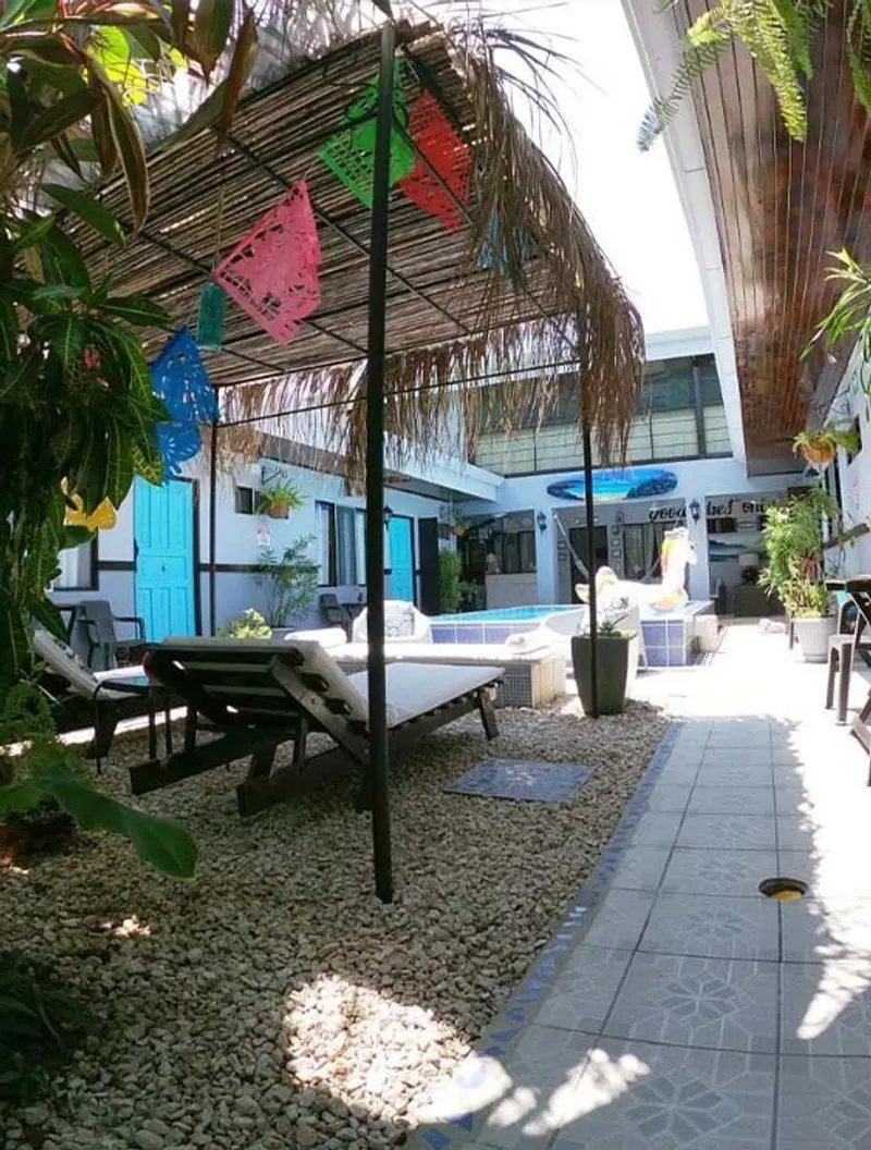 Patio del hotel con camastros, adornos de papel picado colgados y paredes con puertas turquesa