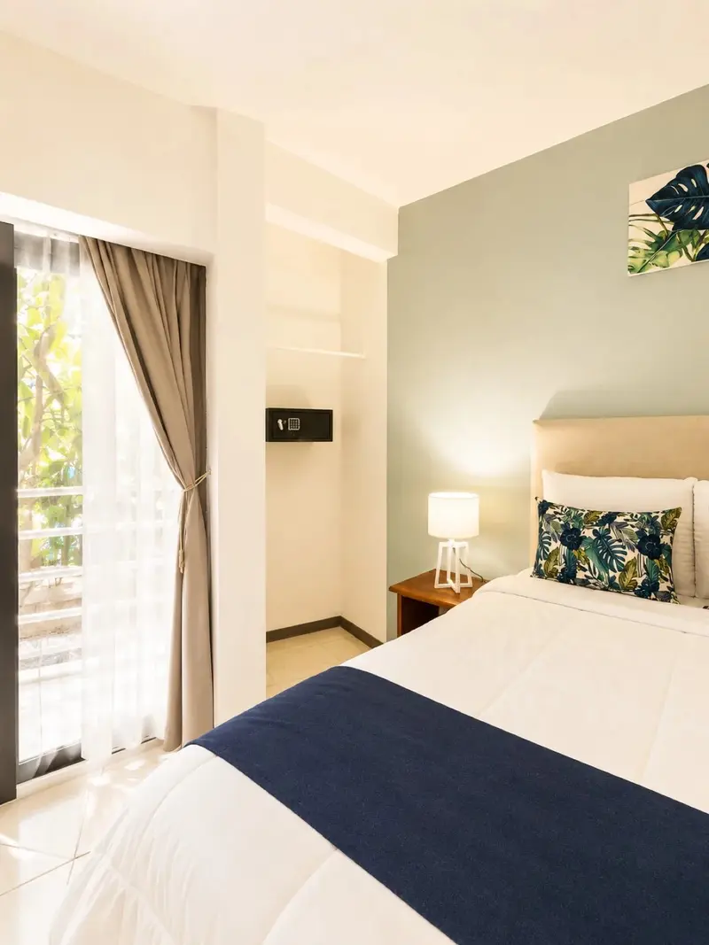 Habitación con cama doble, mesa de noche y puerta de vidrio al balcón