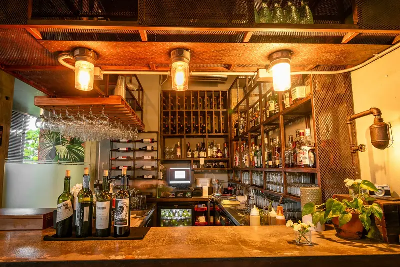 Barra de madera con lámparas colgantes y estantes con botellas de vino y licores detrás