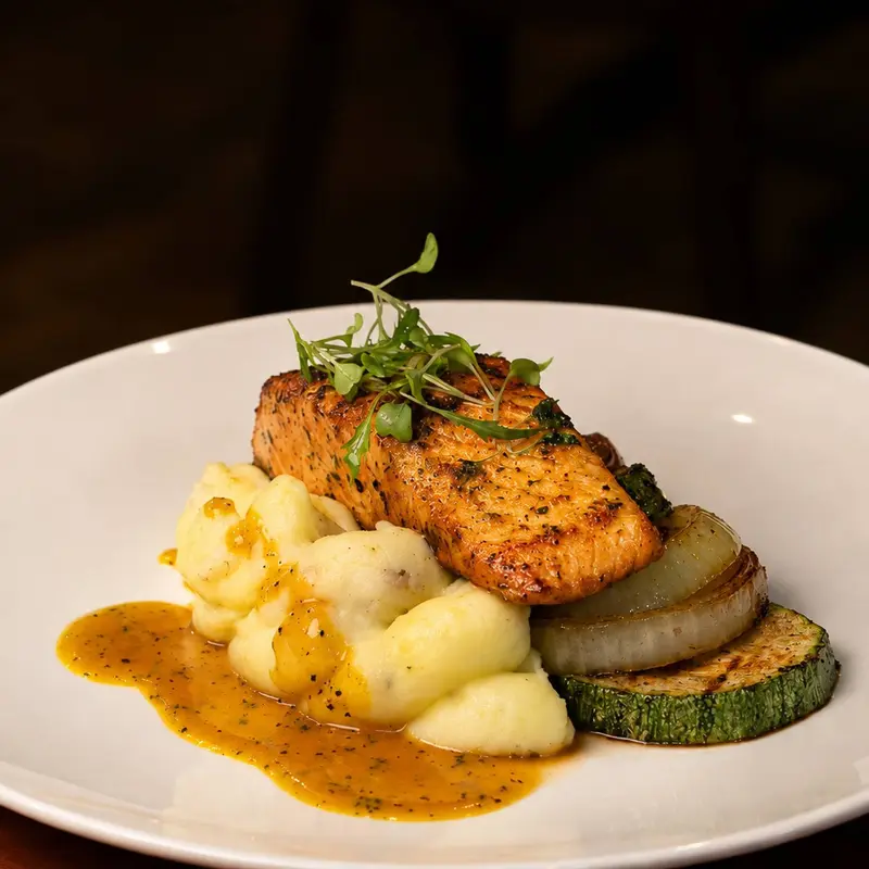 Filete de salmón con salsa amarilla sobre puré de papas, con rodajas de zucchini y cebolla