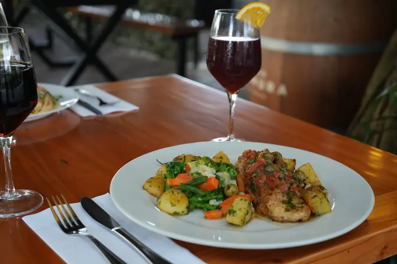 Plato de pollo con verduras salteadas junto a una copa de vino tinto sobre mesa de madera