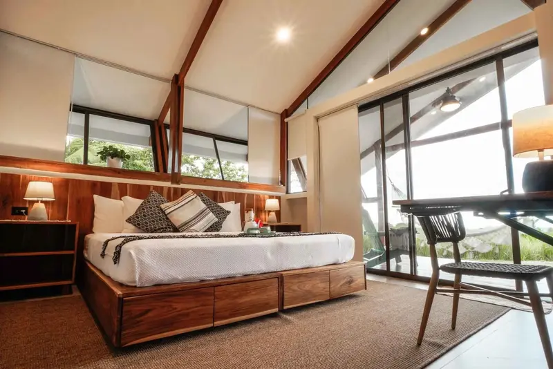 Habitación con cama king de madera, escritorio y grandes ventanales con vista a la montaña