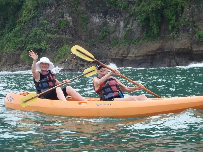Dos personas remando en un kayak naranja frente a un acantilado cubierto de selva
