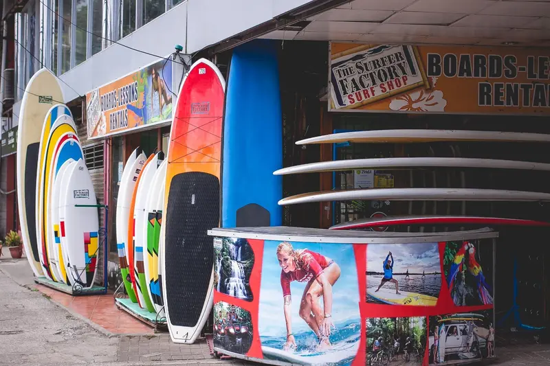 Tablas de surf de colores en la fachada de la tienda, junto a un mostrador decorado con fotos de surfistas
