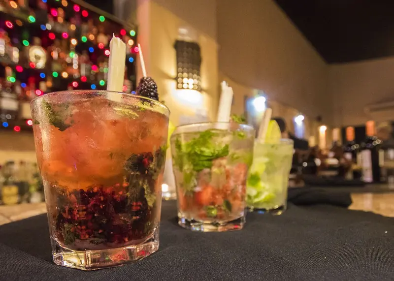 Dos cócteles de frutos rojos y menta sobre la barra, con luces de colores al fondo