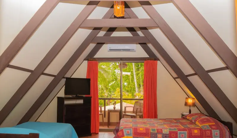 Interior de un bungalow con techo de madera en A, TV y cortinas naranjas frente a una ventana