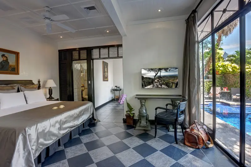 Dormitorio de una suite con cama grande, piso de ajedrez y ventanal con vista a una piscina privada