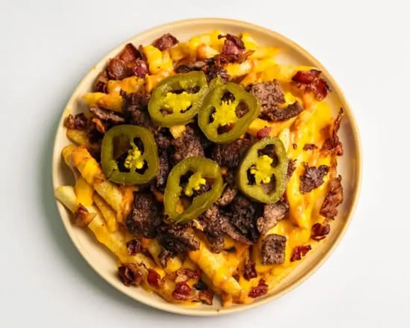 Smash Fries en un plato: papas con salsa de queso, carne en trozos, tocino y rodajas de jalapeño