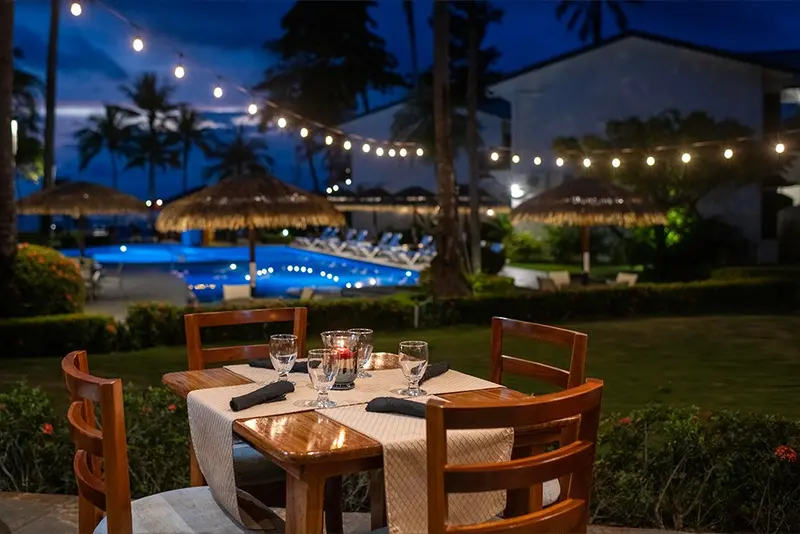 Mesas del restaurante Las Sandalias al anochecer, con luces de cuerda y la piscina al fondo